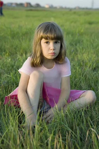 Pequena menina bonito sentado no meio do prado . — Fotografia de Stock