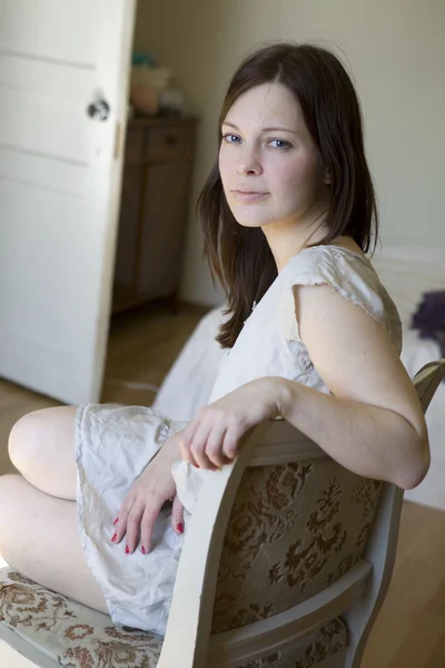 Retrato de mujer morena seria sentada en la silla en la habitación —  Fotos de Stock