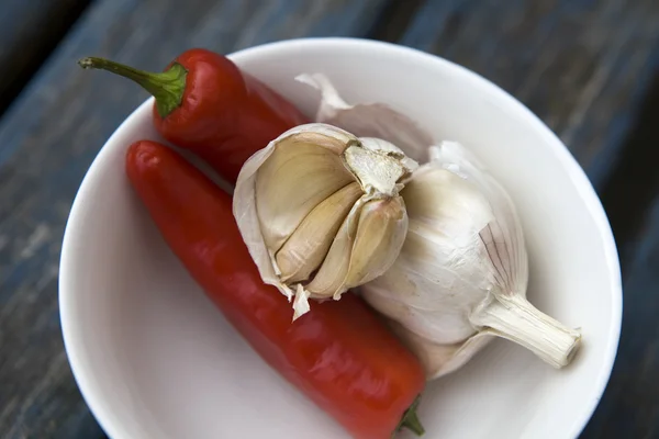 Garlic and traffic light chili pepper in a small round white bowl on blue wooden old table — Stock Photo, Image
