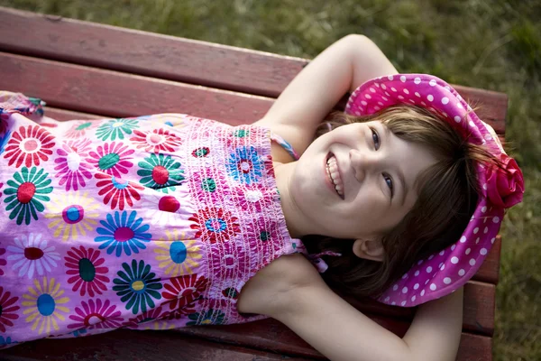 Piccola ragazza carina sorridente di sei anni in panama sdraiata sulla panchina . — Foto Stock
