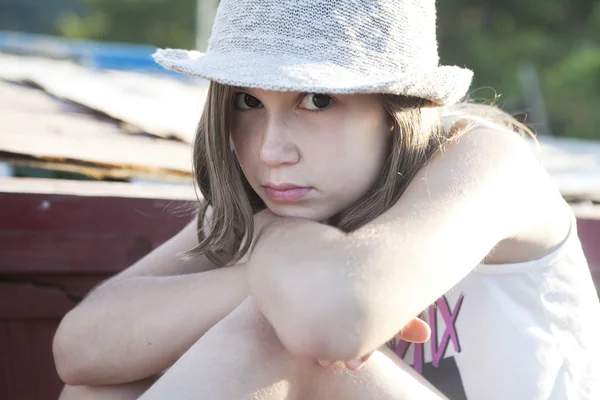 Unhappy little girl in straw hat sitting on chaise longue  on beach — Stock Photo, Image