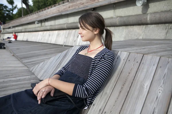 Lonely woman sitting by the river on wooden embankment — Stock Photo, Image