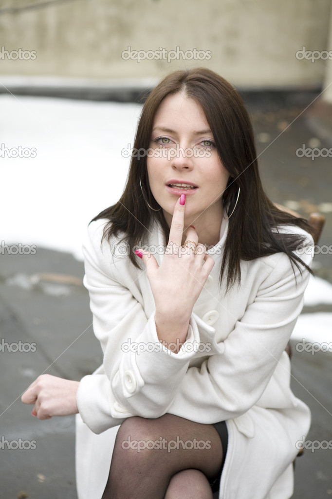 portrait young woman in white overcoat sitting on chair in stree
