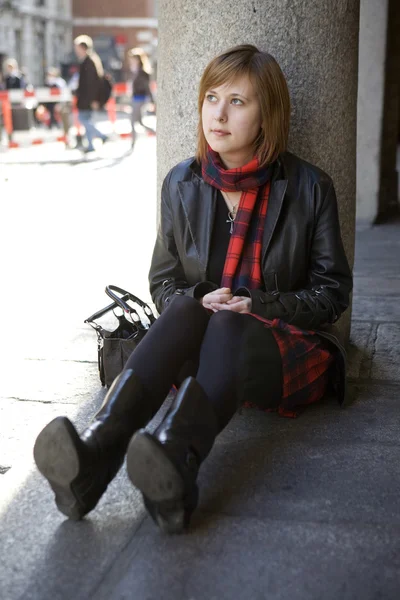 Jovem menina atraente com cabelo vermelho sentado na rua, esperando . — Fotografia de Stock