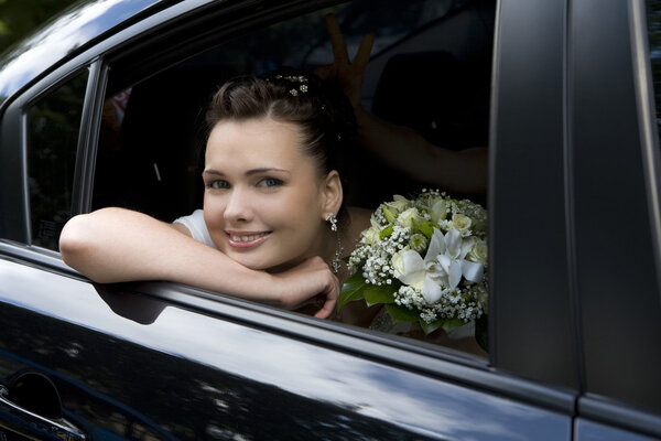 bride with bouquet sitting in wedding car looking through the wi