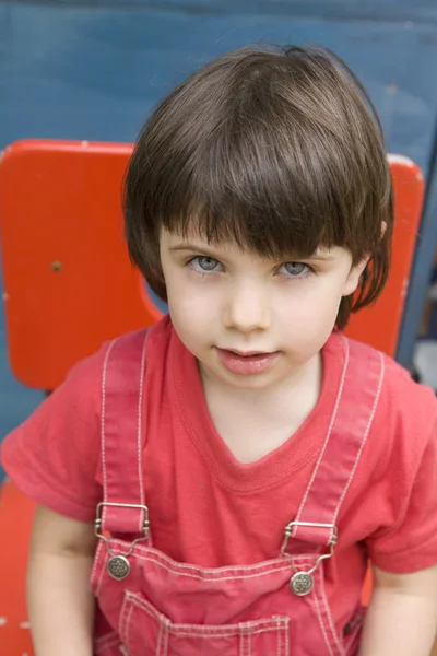 Vážná dívka s modrýma očima v červeným sedí na červené křeslo — Stock fotografie