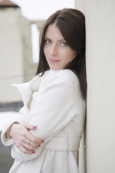 Portrait young attractive woman in white overcoat  standing at w — Stock Photo, Image