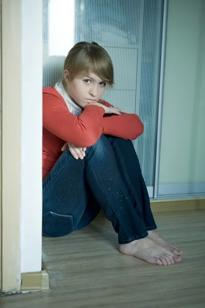 Молодая грустная девушка сидит на углу в комнате. Подростковая проблема — стоковое фото