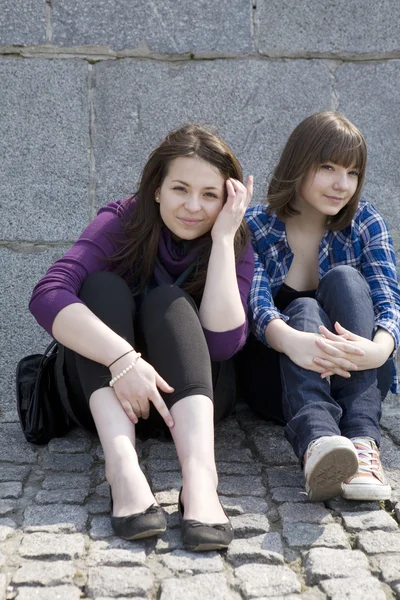 Городские девочки-подростки сидят у каменной стены — стоковое фото
