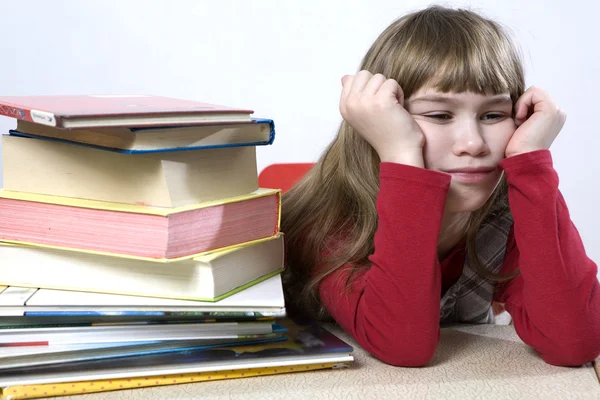 Klein schattig triest meisje met een stapel van boek zitten aan tafel. — Stockfoto