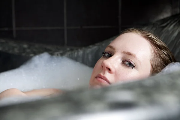 Genç ciddi kadın küvette banyo köpüğü sahiptir. — Stok fotoğraf