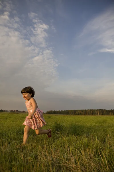 Roztomilý šťastný holčička běží na louce v čas západu slunce. Léto — Stock fotografie