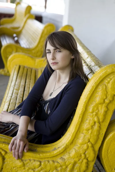 Молодая женщина сидит на желтой скамейке — стоковое фото