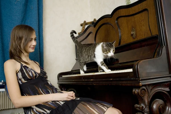 The young woman is watching cat walking on piano — Stock Photo, Image