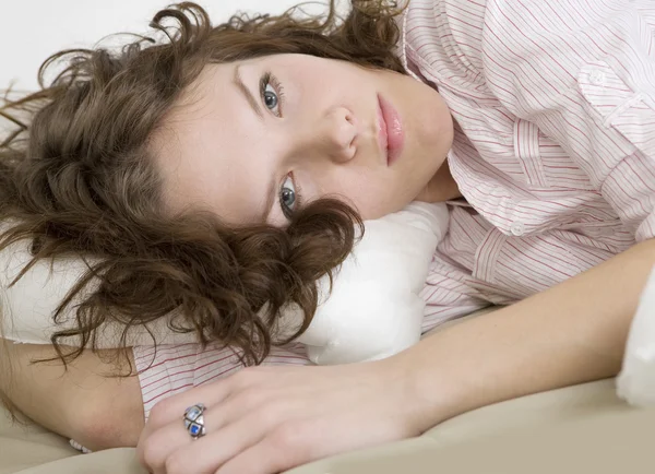 Nachdenkliche brünette lockige Frau, die auf dem Bett liegt — Stockfoto