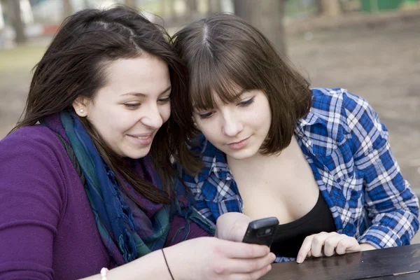 Two teen girls sitting in street cafe lokking at text on mobile phone Stock Photo