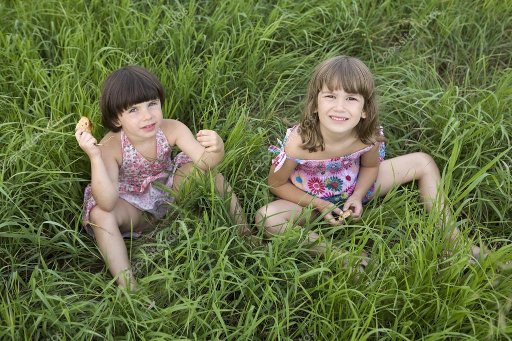 Two girls sitting in the grass in meadow. 