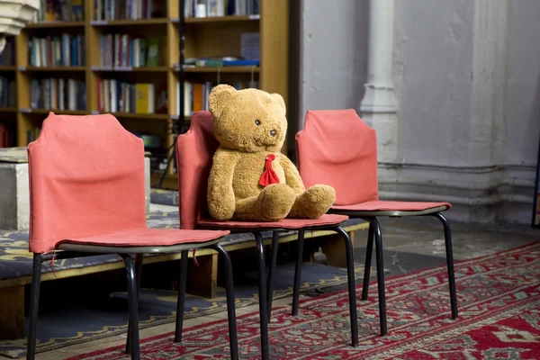 Starý medvídek sedící na židli v místním kostele na místě pro děti — Stock fotografie