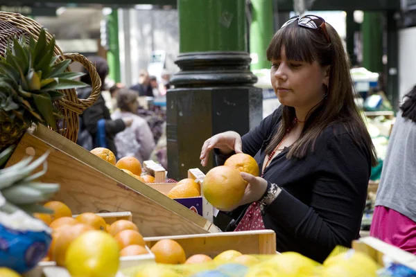 Ung kvinna köpa orange på Borough market — Stockfoto