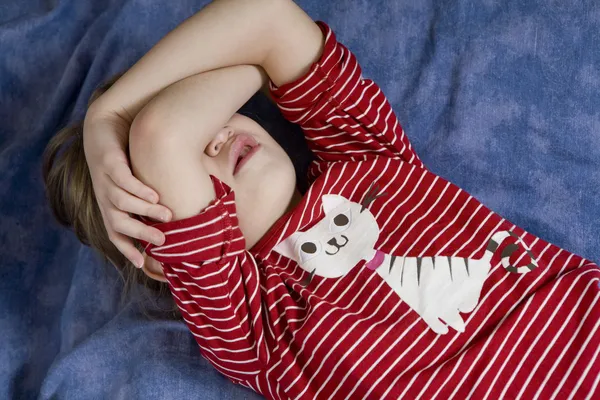 Mała dziewczynka leżąc na łóżku zamknięcia fase przez ręce noszenie koszuli dowcip — Zdjęcie stockowe