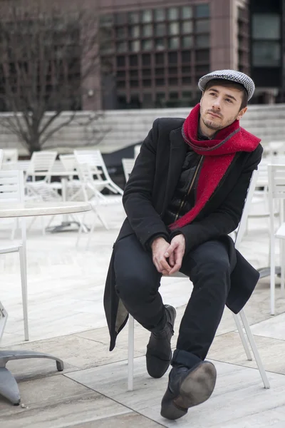 Young sad man wearing check cap sitting at the street cafe waiting for order — Stock Photo, Image