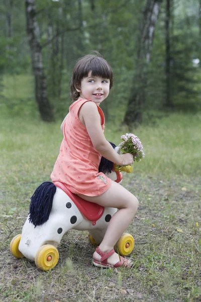 Mała dziewczynka uśmiechający się jeździć konia zabawka — Zdjęcie stockowe