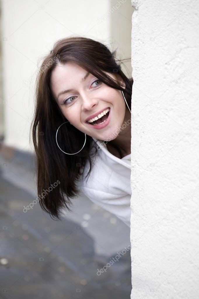 attractive young woman  peeking around the corner at house 