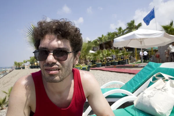 Человек в солнечных очках сидит на пляже — стоковое фото