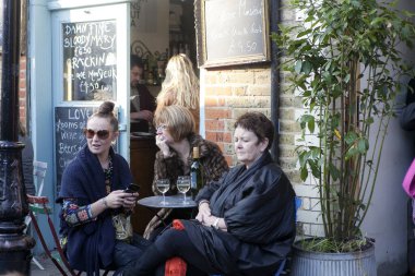 Londra, İngiltere - 20 Kasım 2019, Üç yaşlı kadın bir sokak kafesinde bir masada oturuyor, kahve içiyor, sokak müzisyenlerini dinliyorlar.