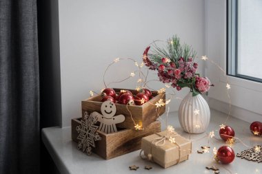 Sarmaşık yaprakları, elmalar ve dikenli meyvelerle süslenmiş yapay bir ladin dalı. Ahşap kutuda yanan mumlar, kırmızı cam toplar, kış kompozisyonu Noel arifesinde iç dekorasyonlar yapar.