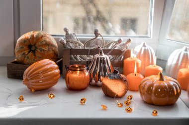 Porselen ve doğal balkabakları, beyaz bir masada turuncu mumlar, Cadılar Bayramı süslemeleri..
