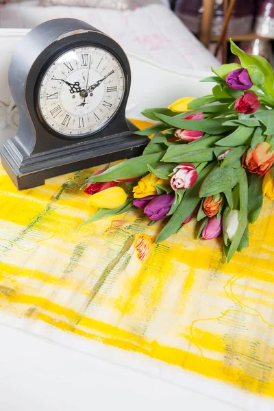 古いテーブルクロックの横にあるテーブルの上には 色とりどりのチューリップの花束があります — ストック写真