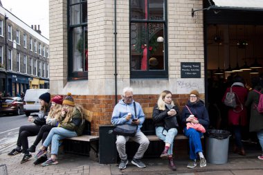 Londra, İngiltere - 20 Kasım 2020, İnsanlar bir kafenin yanındaki bankta oturup kahve içiyorlar.