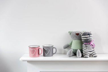 Beyaz kalbi boyalı pembe ve gri bir kupa şöminenin üzerinde iki komik oyuncak kedi duruyor. Sevgililer Günü için ev dekorasyonu. İskandinav tarzı