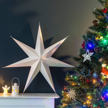 Noel 'den önce ev dekorasyonu. Süslü Noel ağacı, çelenk ışıkları, sallanan at, zarif kağıda sarılmış hediyeler, büyük beyaz bir yıldız ve mumlarla suni şömine..