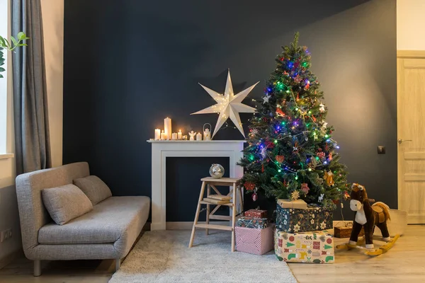 圣诞节前的家居装饰装饰圣诞树 装饰着花环灯 摇曳的马 精美的纸包裹着的礼物 用大白纸星和蜡烛装饰的人造壁炉 — 图库照片