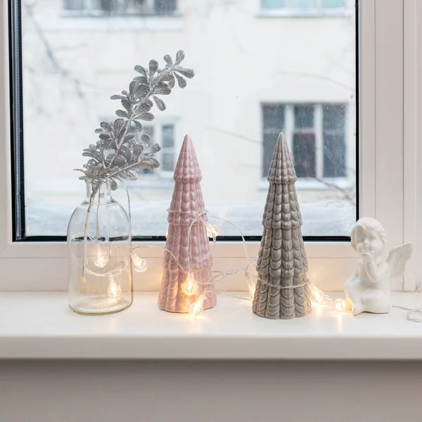 圣诞前夕 灰色和粉色的陶瓷圣诞树 一个装有人造银枝的玻璃瓶和一个装饰窗台的花环装饰着圣诞 — 图库照片