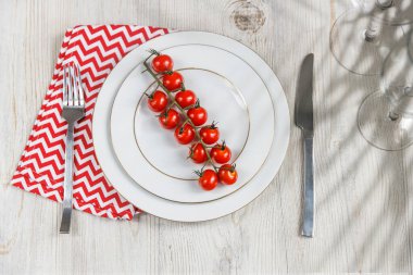 Servis tabağı, kaşık, çatal, bıçak ve kırmızı peçete ahşap masada. Kilo verme ve diyet kavramı. İki büyük tabakta domates.