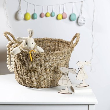 Paskalya için iç dekorasyon. Bir paçavra tavşanı masanın üzerindeki hasır bir söğüt sepetinden bakıyor. Üzerinde boyanmış yumurtalardan oluşan bir çelenk.