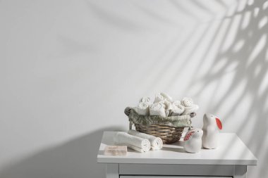 Yuvarlak yüz havluları, sabun ve çekmecede iki seramik tavşan figürü olan bir hasır sepet. Palmiye yaprağının gölgesi. Paskalya için banyo dekorasyonu. Metin için yer