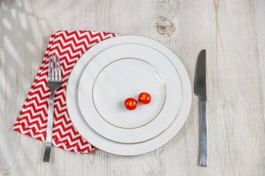 Servis tabağı, kaşık, çatal, bıçak ve kırmızı peçete ahşap masada. Kilo verme ve diyet kavramı. İki büyük tabakta domates.