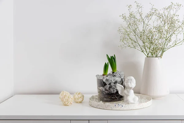 Gypsophila in a ceramic vase, hyacinths in a glass vase on a white dresser. View of modern scandinavian style interior. Living room, commode with vases. Minimalism concept
