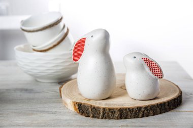 Kırmızı kulaklı iki beyaz tavşan heykeli büyük ve küçük tahta testereyle kesilmiş ve arka planda yumurta dolu bir kase beyaz İskandinav tarzı mutfakta.