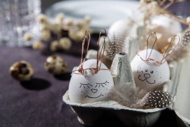 Paskalya konsepti. Bakır kablo kulaklı beyaz bir yumurta ve kutuda uyuyan boyalı bir tavşan yüzü. Keklik yumurtası ve tüyleri..