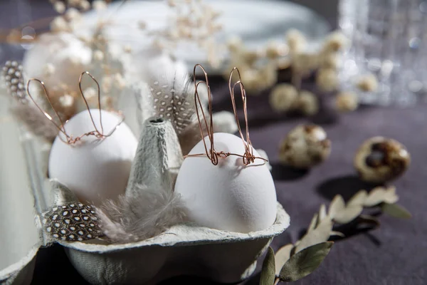 Paskalya konsepti. Bakır kablo kulaklı beyaz bir yumurta ve kutuda uyuyan boyalı bir tavşan yüzü. Keklik yumurtası ve tüyleri..