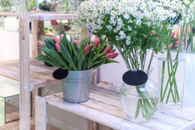 Çiçekçide satılık bir kova dolusu beyaz, kırmızı lale ve papatya..