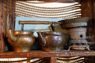 Eski bir evdeki mutfağın iç dekorasyonu. Bakır çaydanlık, su testisi, kızartma tavası ve ahşap bir rafta gazyağı sobası..