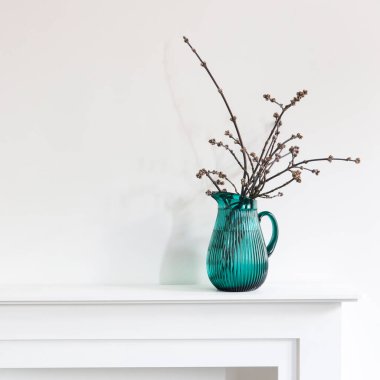 Kavak dalları kesilmiş yeşil bir sürahi beyaz bir şöminenin üzerinde oda dekorasyonu olarak duruyor.