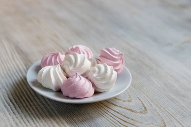 Beyaz bir tabakta bej bir masada beyaz ve pembe şekerlemeler.