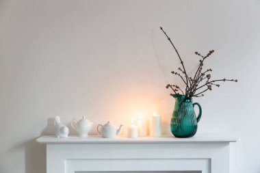 Yeşil cam bir kavanozda Amerikan akçaağaç dalları, porselen bardaklar, biblolar, beyaz bir çekmecede çaydanlık. İskandinav tarzı